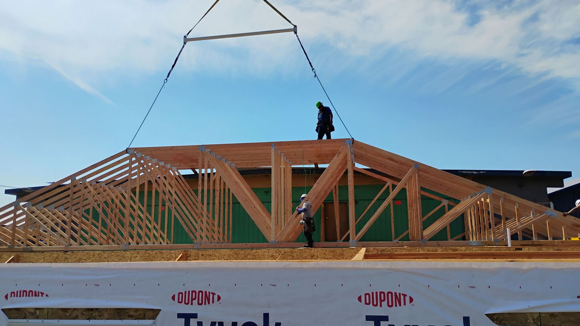 Roof truss lift with two workers on a commercial building, DuPont Tyvek wrap visible