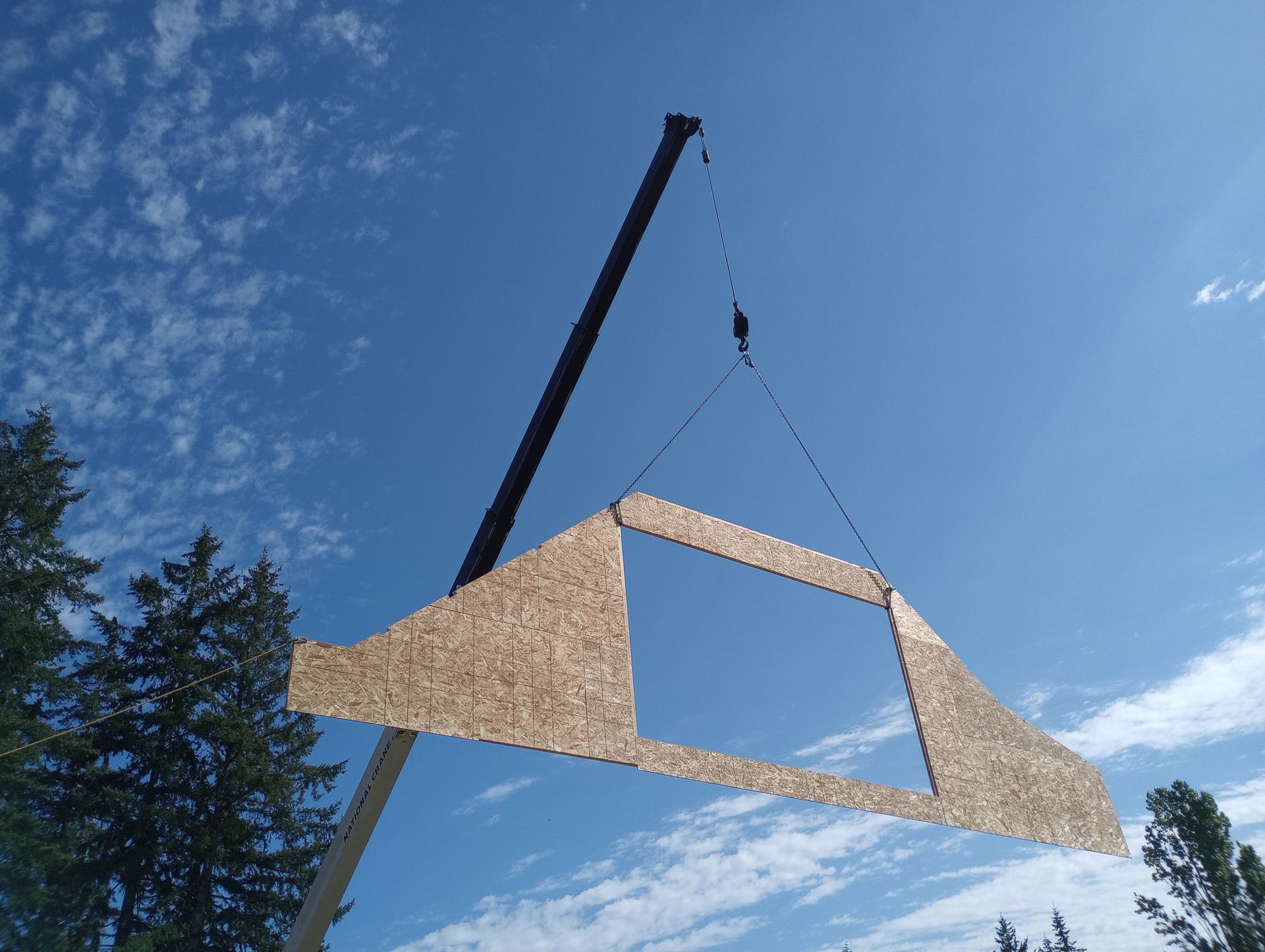 Gable-end wall panel suspended by chain rigging against open sky