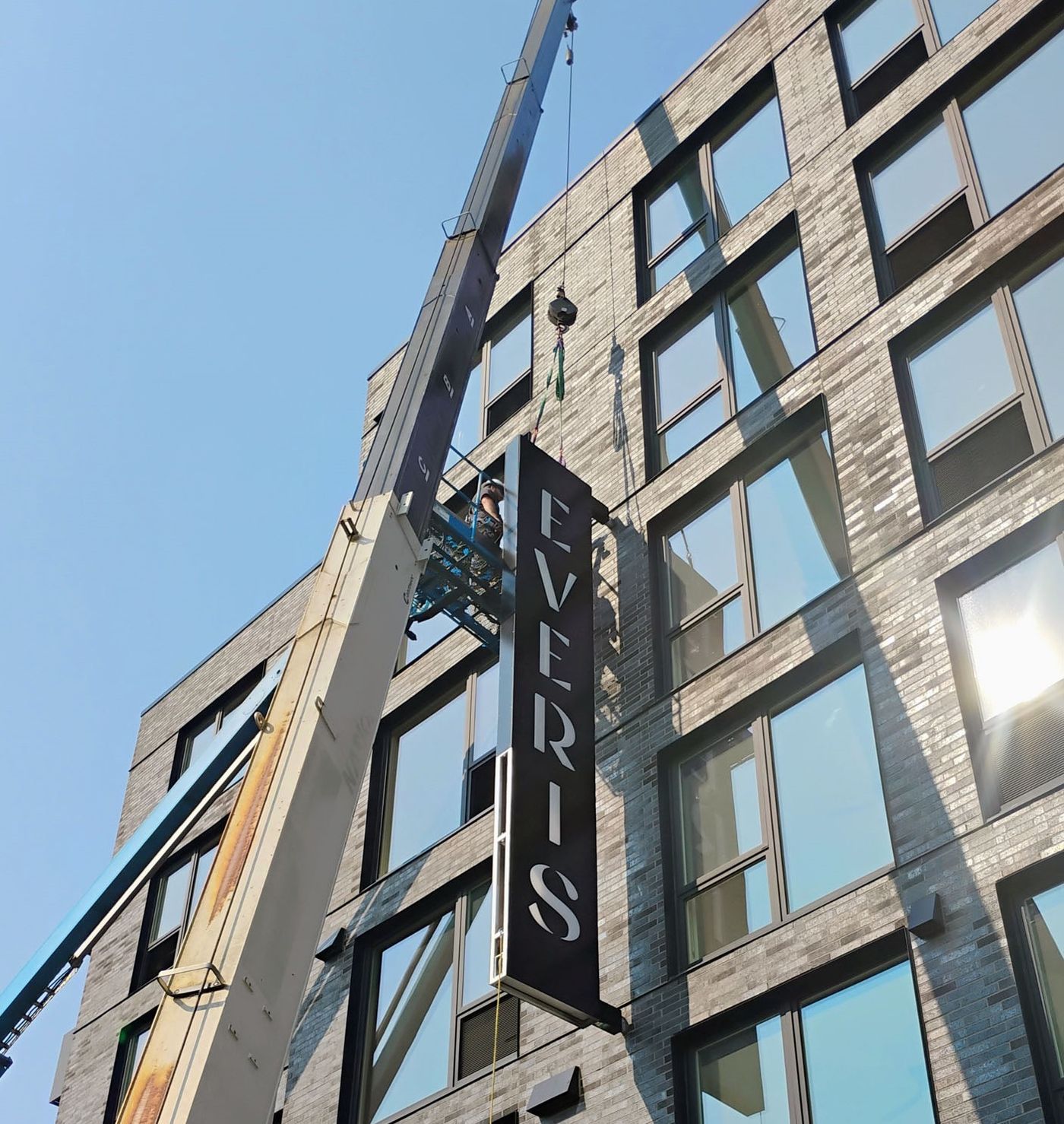 Crane boom and lift basket installing a commercial building sign
